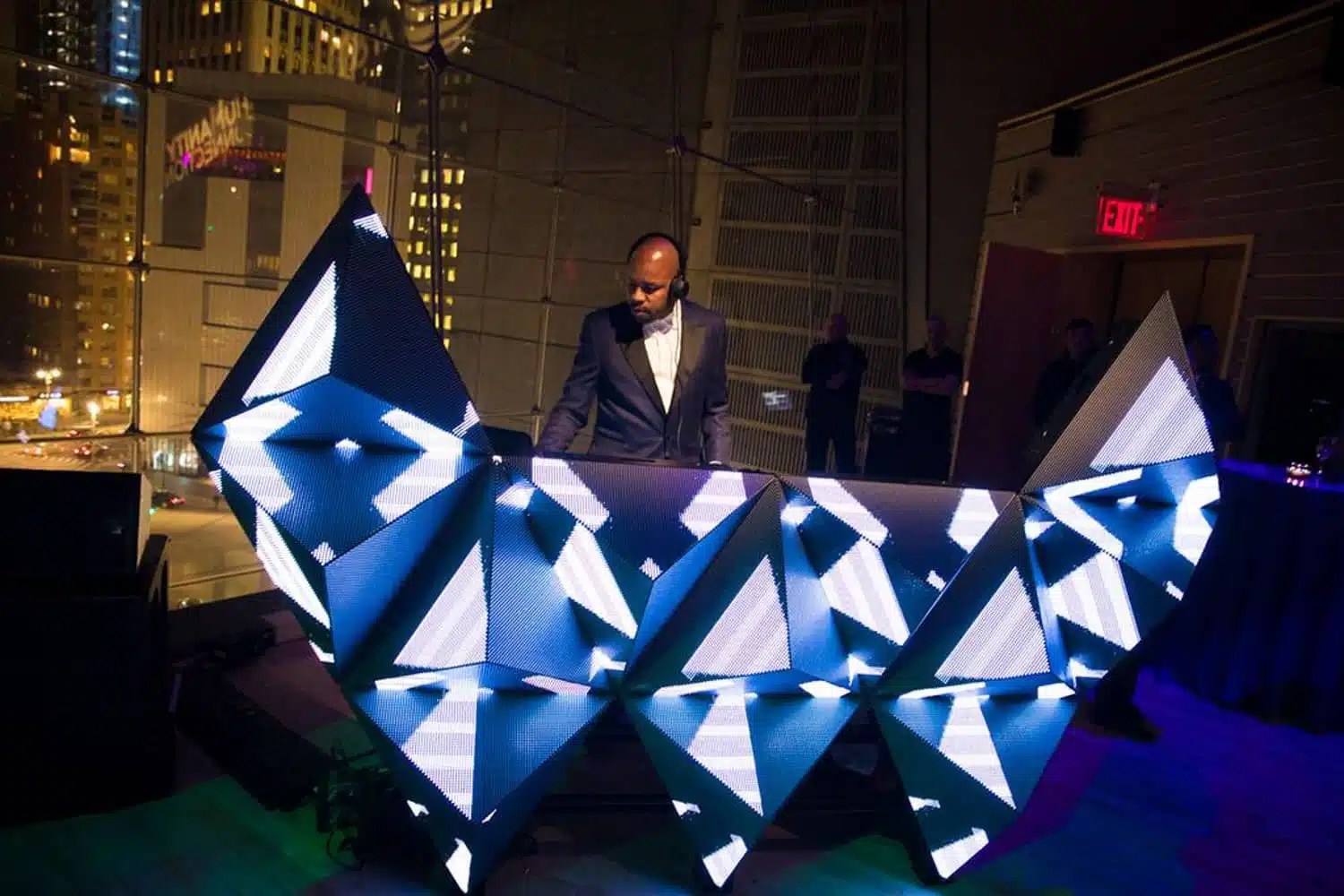 DJ at a visually striking LED booth with geometric patterns, set in a vibrant event space, highlighting Event Fab's innovative rental offerings for immersive experiences.