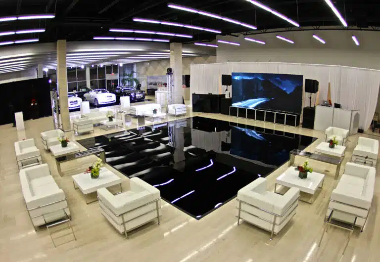 Lounge furniture rental setup featuring white sofas and coffee tables arranged around a reflective black dance floor, creating a modern event space for social interaction and comfort.