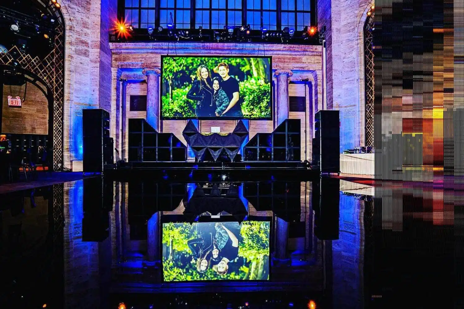Professional audio-visual setup featuring large LED screen displaying a family portrait, surrounded by sound equipment and dramatic lighting, ideal for events like weddings and conferences.