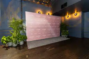 Event signage backdrop with pink branding, potted plants, and a wooden floor, designed for enhancing event experiences.